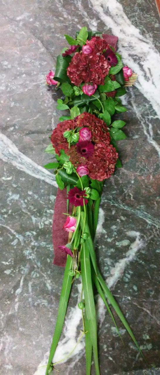 Rouwarrangement gemaakt op rietstengels liggend op vilt. 
Bloemen: hortensia's, rozen, gerbera's, sedum.